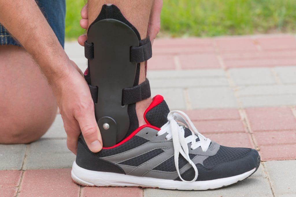 Man in athletic sneakers checking his ankle orthosis or brace on the street